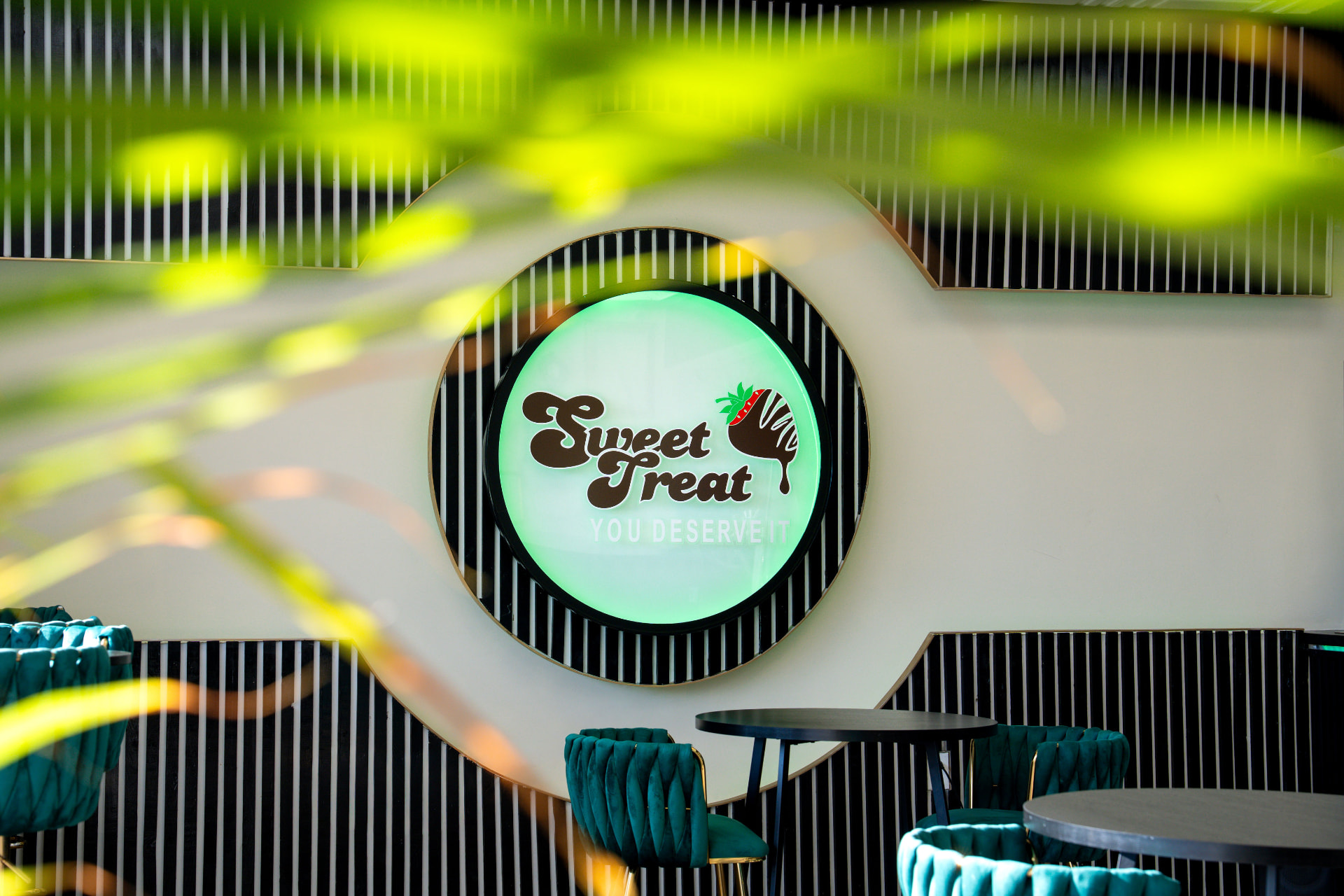 Sweet Treat café with its glowing logo, curved wall, and teal chairs